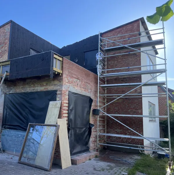 Muret facaderenovering med mørk klinker og stillads under udførelse