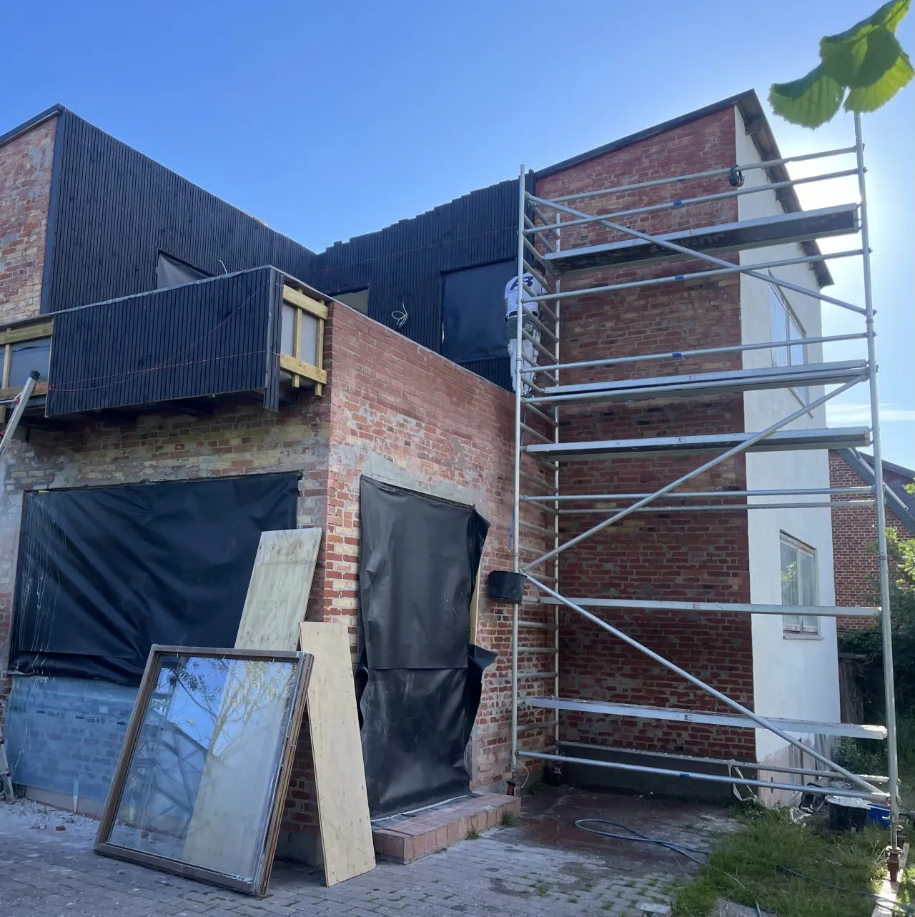 Muret facaderenovering med mørk klinker og stillads under udførelse